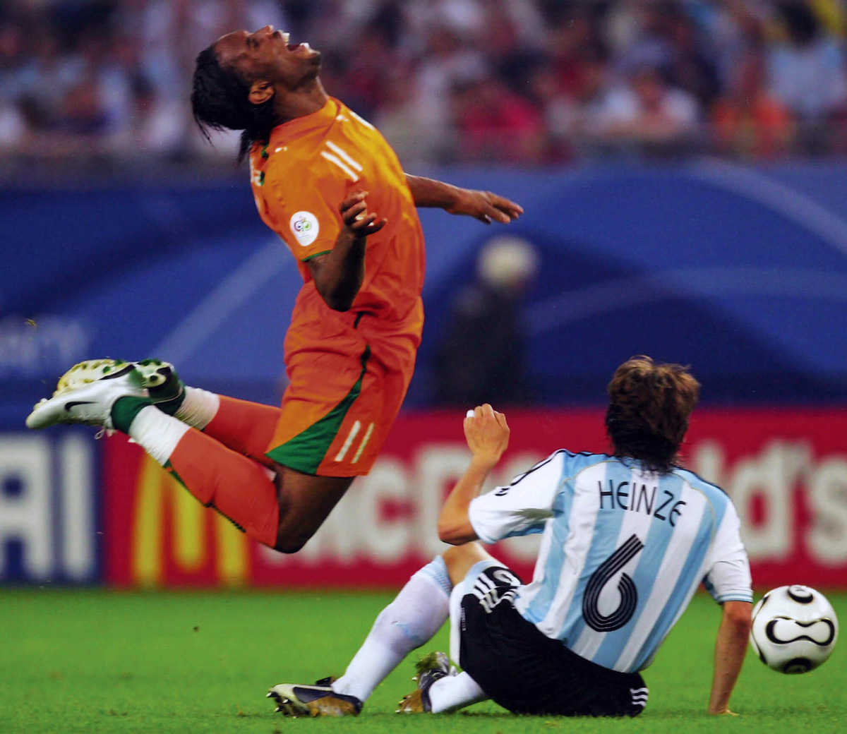 A photograph of the Ivory Coast’s Didier Drogba demonstrating a classic “archer’s bow” as he is tackled by Argentina’s Gabriel Heinze in the two thousand and six World Cup.