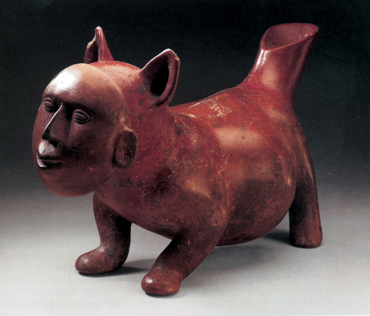 A photograph of a figurine of an escuincle wearing a mask with a human face. 