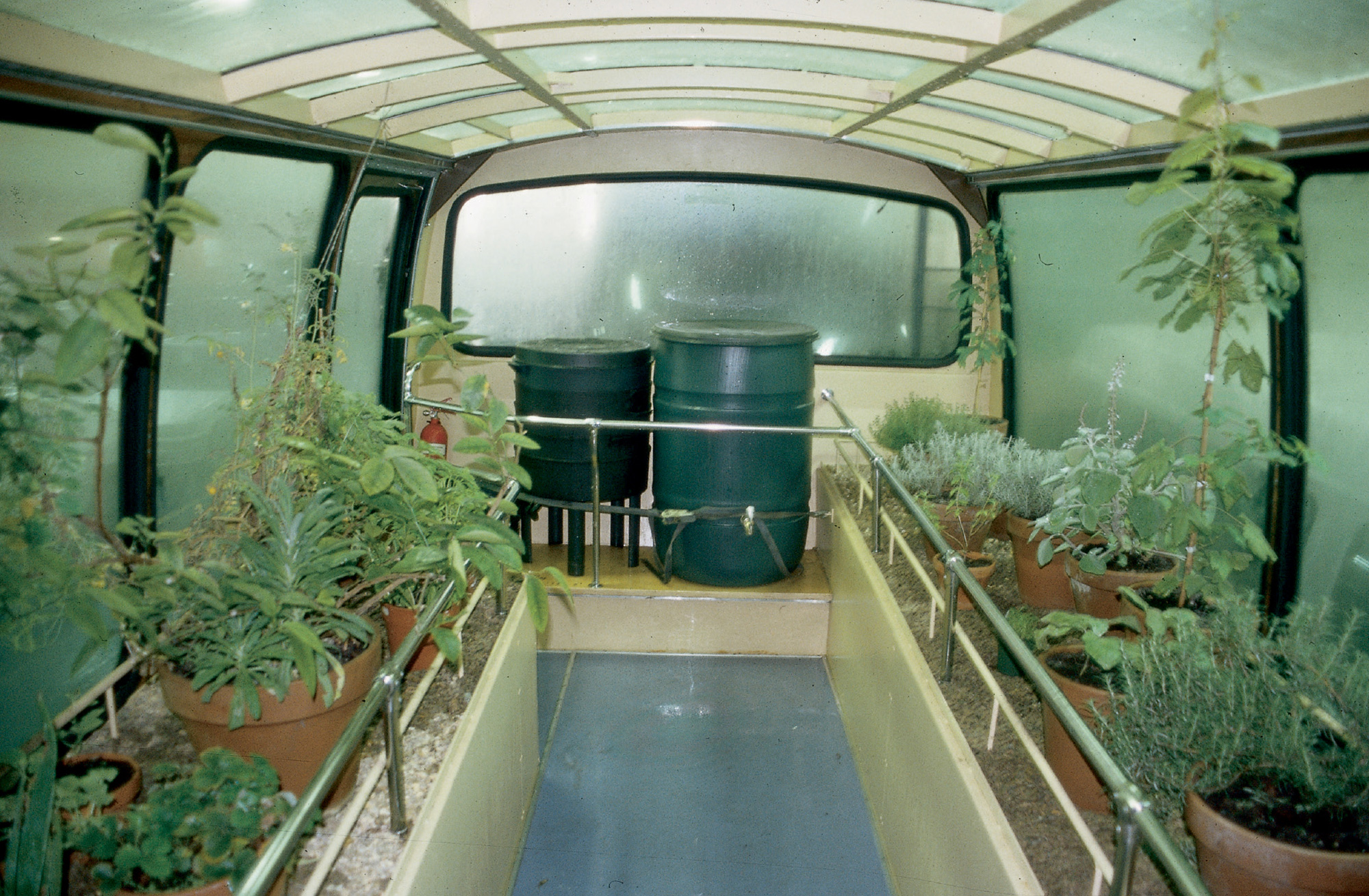 An image from an artwork entitled “Proposed Redevelopment of the Oval, Hackney E2, London” showing the interior of a bus reconfigured as a mobile greenhouse filled with growing plants.