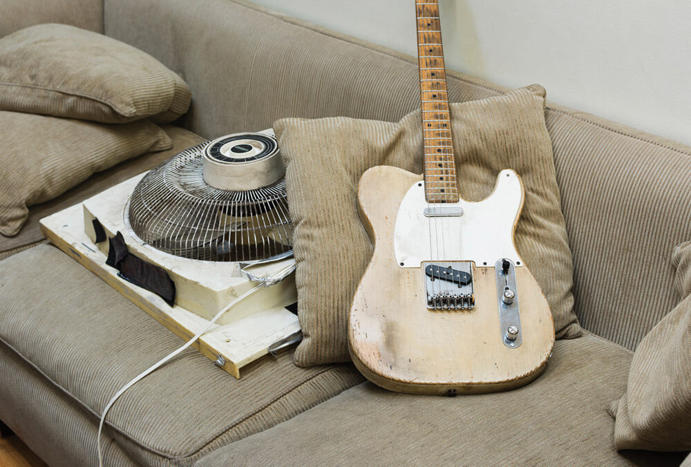 A photograph of a wooden electric guitar resting on a sofa.