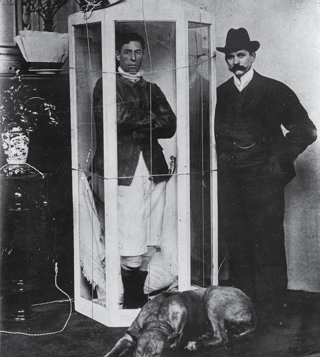 A photograph of hunger artist Papus, who was active around the turn of the twentieth century, in his sealed glass box at the Passage-Panoptikum in Berlin.