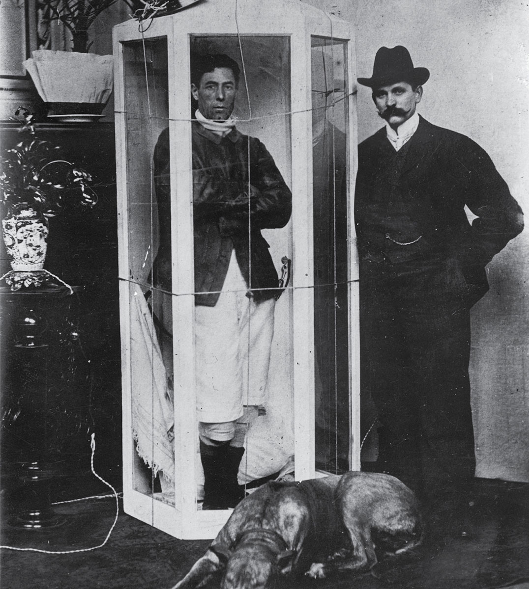 A photograph of hunger artist Papus, who was active around the turn of the twentieth century, in his sealed glass box at the Passage-Panoptikum in Berlin.