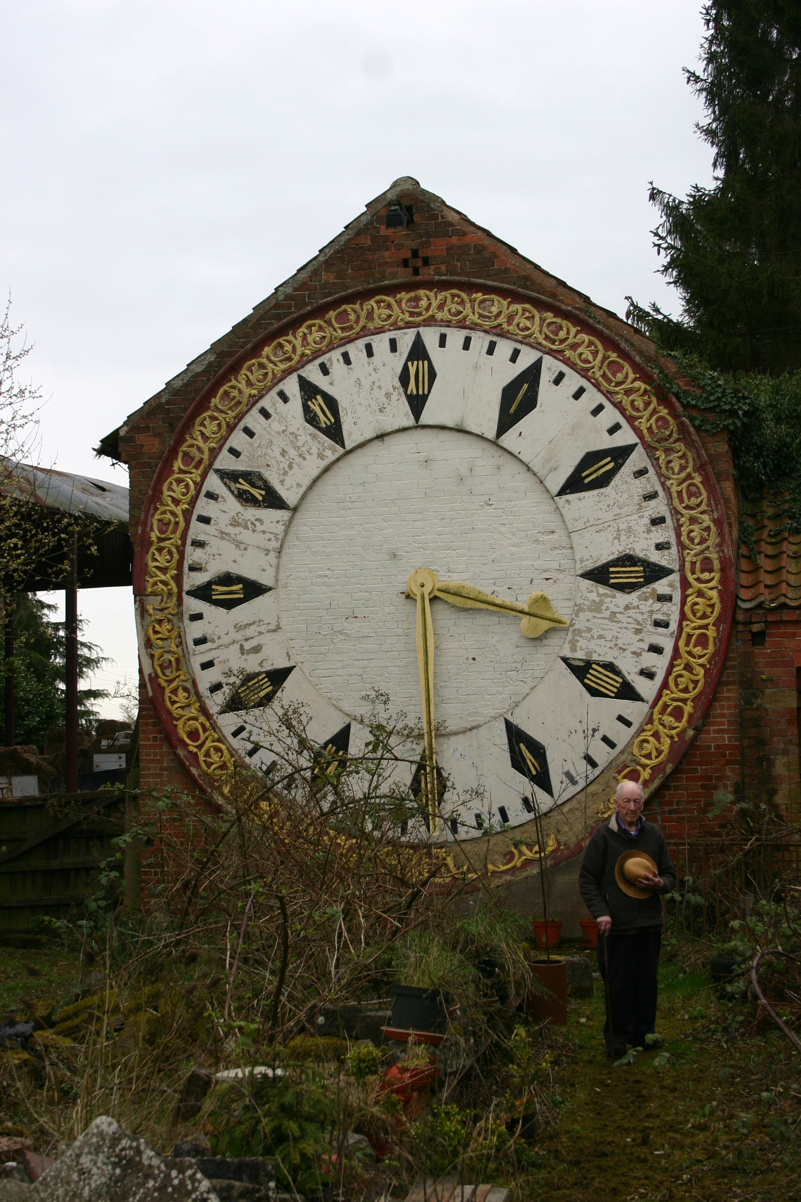 A photograph of Roland Hoggard in front of the restored St. Pancras railway station clock installed on a wall in his garden.