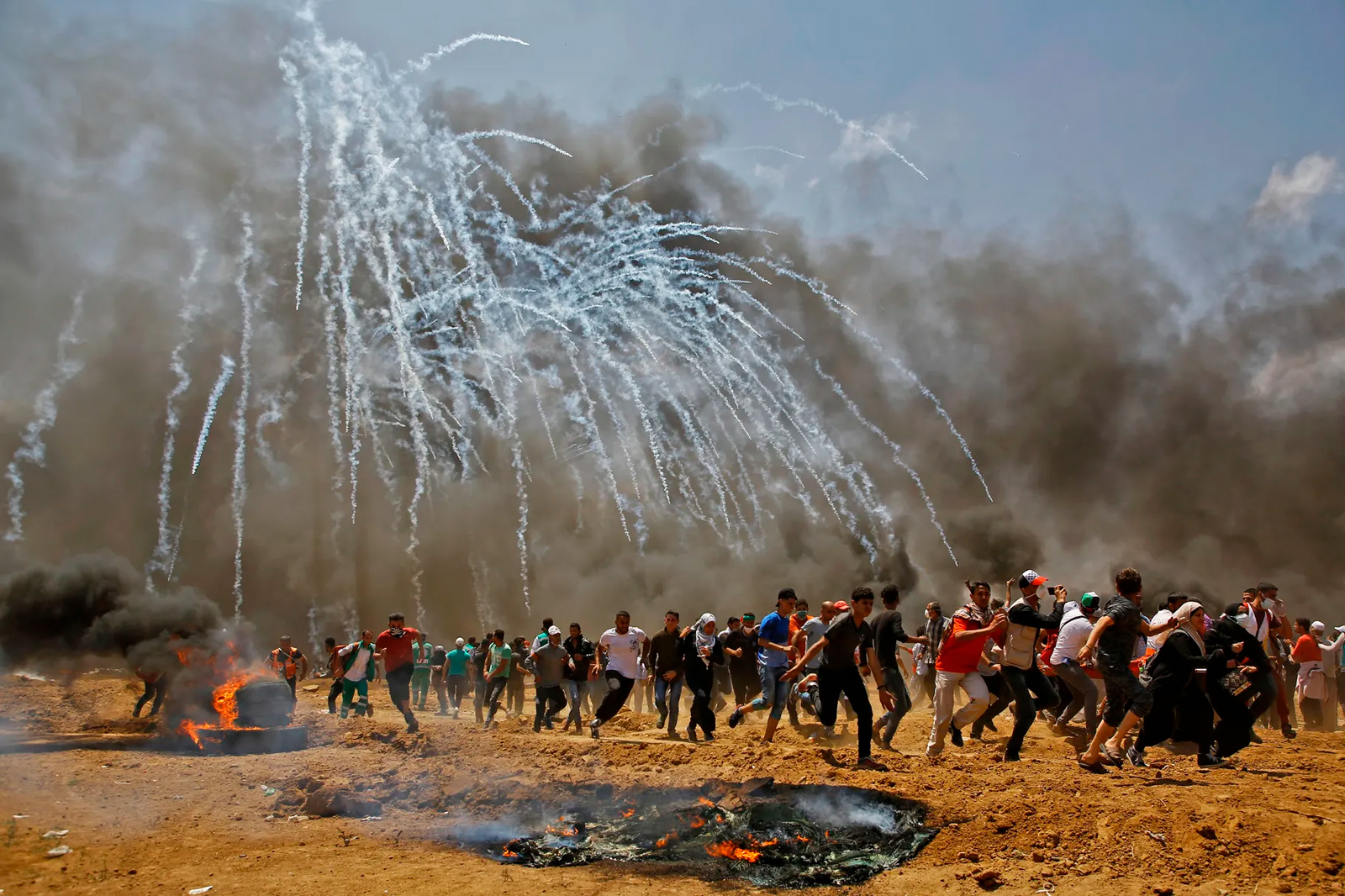 Israeli soldiers firing tear gas at Palestinians, Gaza City, 14 May 2018. The protest was part of the months-long Great March of Return demonstrations. In its “Report of the Independent International Commission of Inquiry on the Protests in the Occupied Palestinian Territory,” the UN Human Rights Council determined that between 30 March 2018 and the end of the year, Israeli soldiers killed 189 Palestinians demonstrators, including 35 children, 2 members of the press, and 3 health workers. In addition, some 9,000 Palestinians were injured, the vast majority as a result of live ammunition. Photo Mohammed Abed.