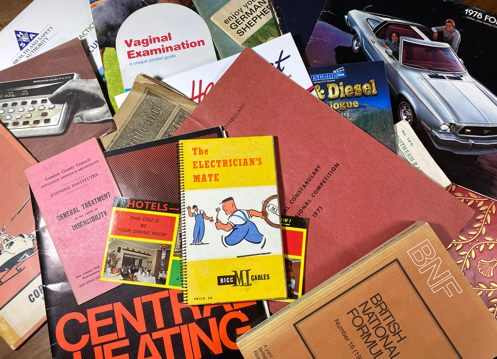Photograph of various gray literature books and pamphlets, including a title called “The Electrician’s Mate,” messily arrayed on a table.