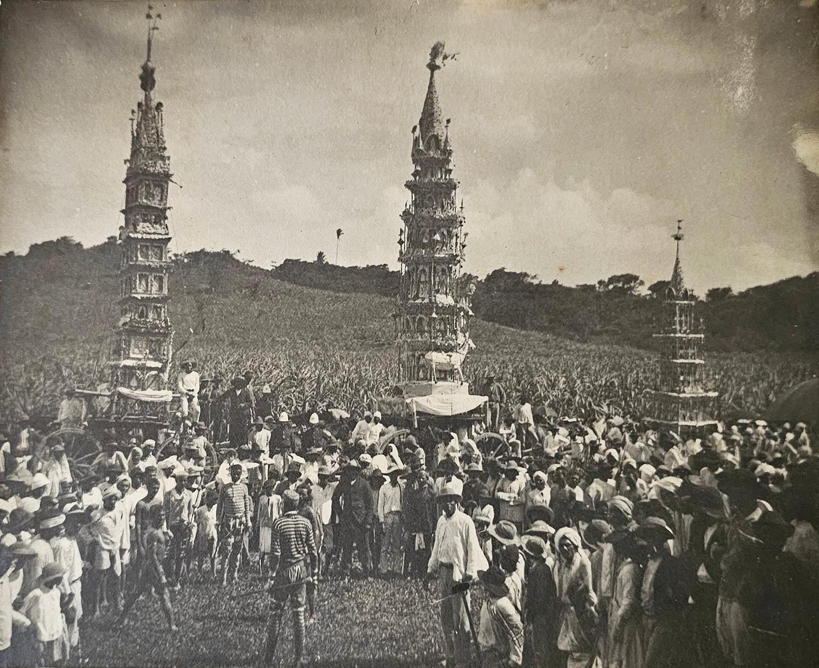 A late-nineteenth-century photograph, possibly taken after the eighteen eighty-four massacre, depicting Trinidadians celebrating the Hosay ritual. The photograph features intricate tiered structures known as “tadjah,” which represent the tomb of Imam Hussain.