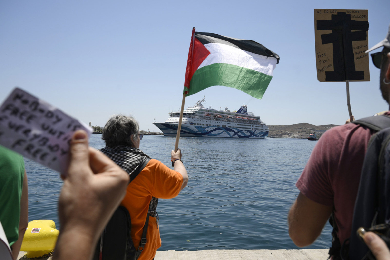 A woman holding a Palestinian flag in Syros. In the background, the Crown Iris cruise ship is visible.