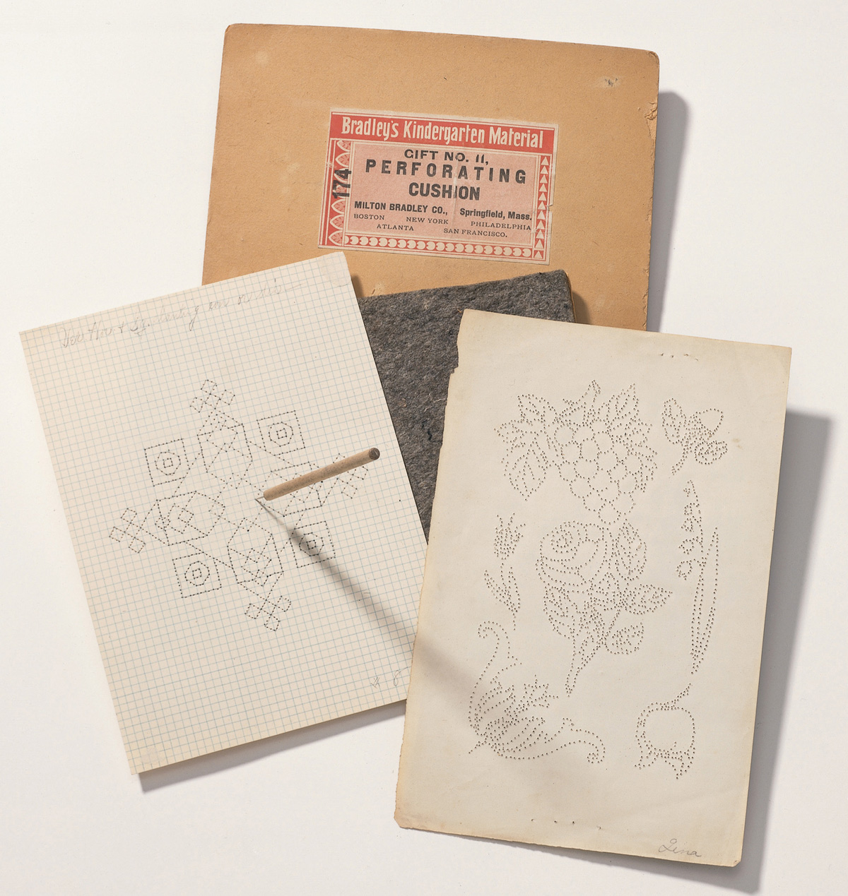 A photograph of perforating cushions manufactured by Milton Bradley Company, and two paper pricking exercises by a teacher and a kindergartner made using them, United States, circa 1900.